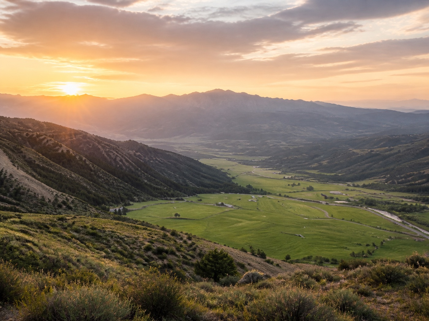 Open valley ranchland at sunrise with mountains in the distance